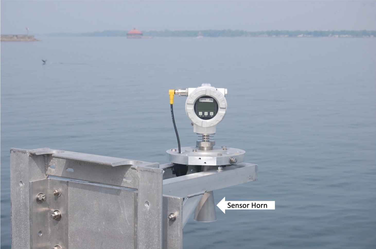 Microwave water level sensor mounted on a metal platform over the water. Arrow pointing to sensor horn is shown undeter the platform.